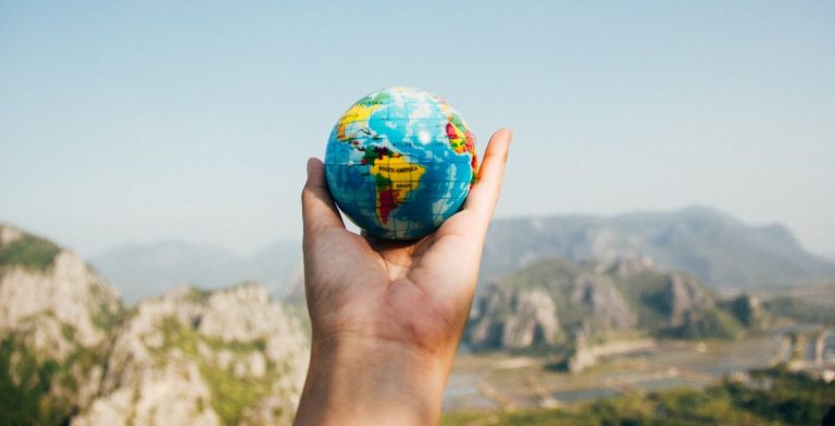 A hand holding a tiny globe against a blurry view of mountain cliffs.