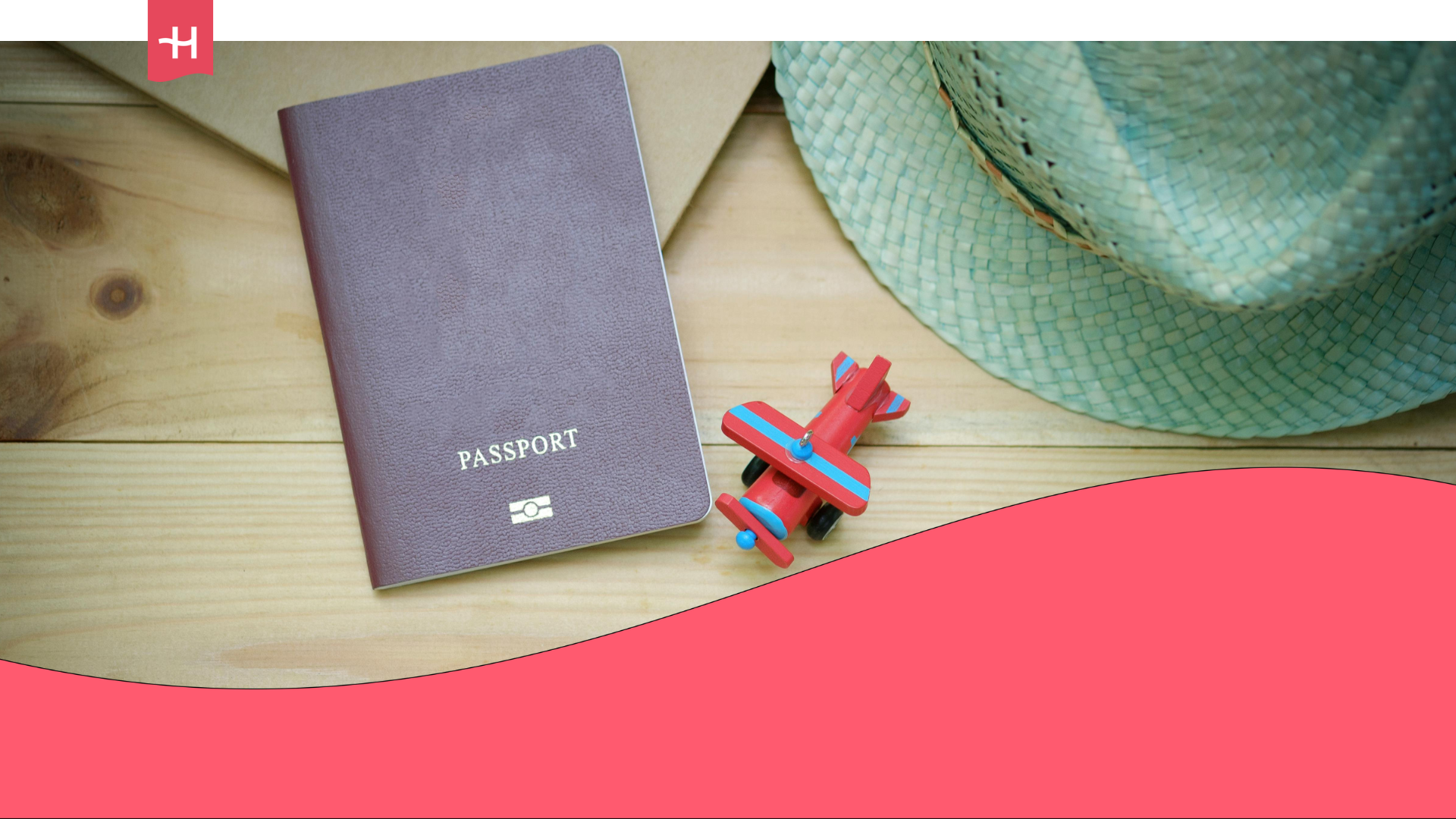 A passport is placed on a wooden table, next to a red toy plane and a green straw hat.