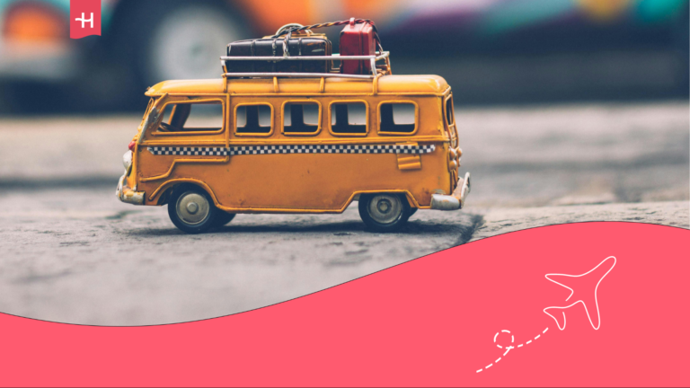 A yellow toy bus is placed on a sidewalk, with several colorful miniature suitcases stacked neatly on its roof. The playful scene gives off a sense of travel and adventure, as if the tiny bus is packed and ready for a trip.