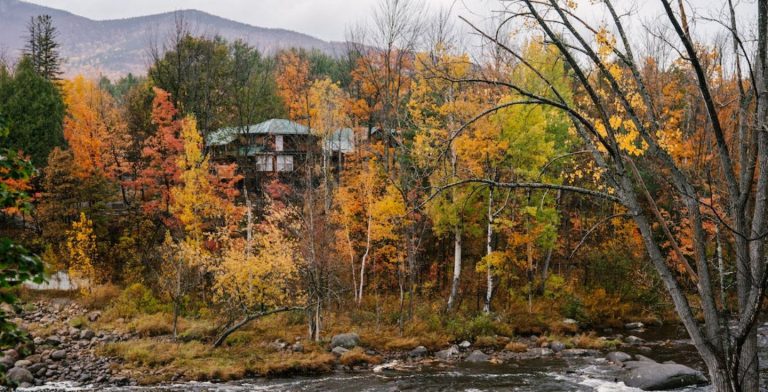 Rusty fall foliage surrounding a cabin by a rocky riverbed.