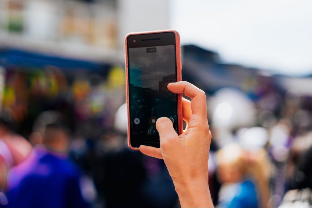 A hand holding a phone in front of a blurred crowd of people