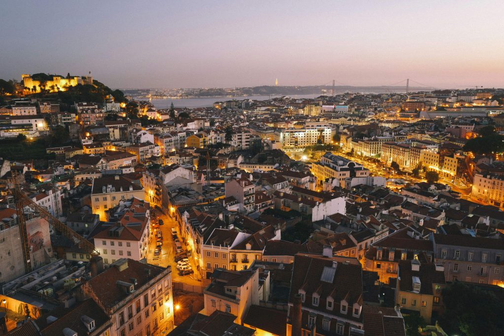 Lisbon shot from a viewpoint on the outskirts, capturing the city lit up by street lights on a warm evening.