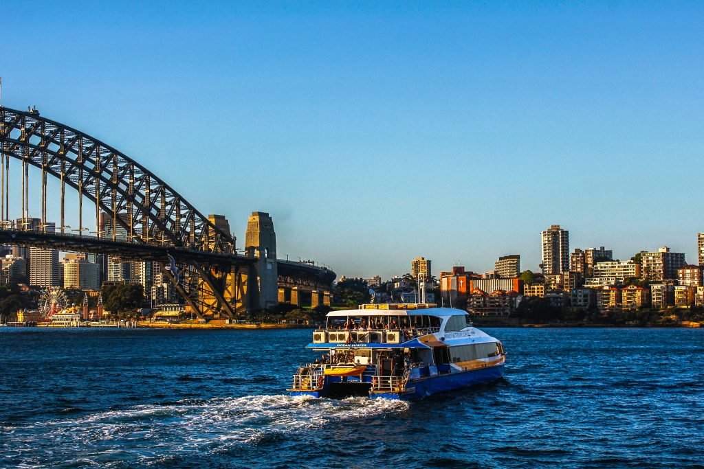 A boat tour carrying tourists cruises past Sydney Harbour Bridge. 