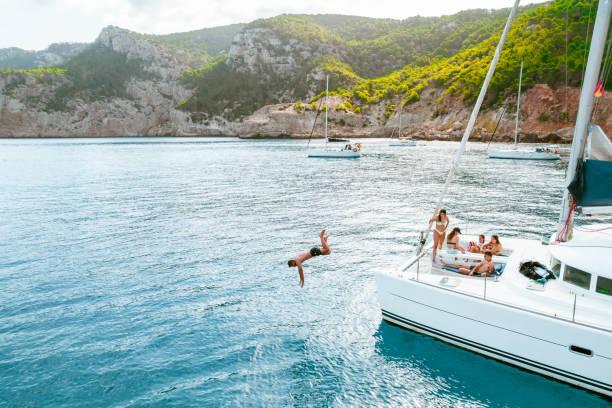 A group of friends relaxing on a catamaran in Ibiza with one of them diving into the sea.