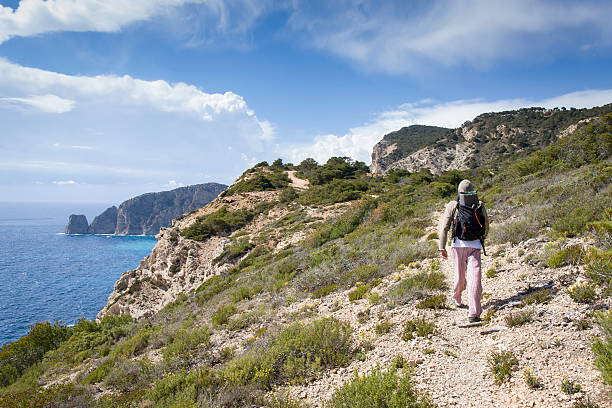 A lone tourist wearing a backpack hiking along the coastline in Ibiza