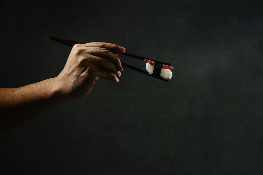 A hand holding chopsticks with a roll of sushi inside