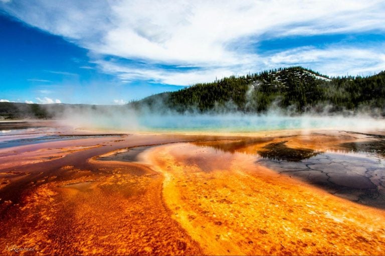 Geothermal pools in Yellowstone National Park with snow-dusted mountains in the background.