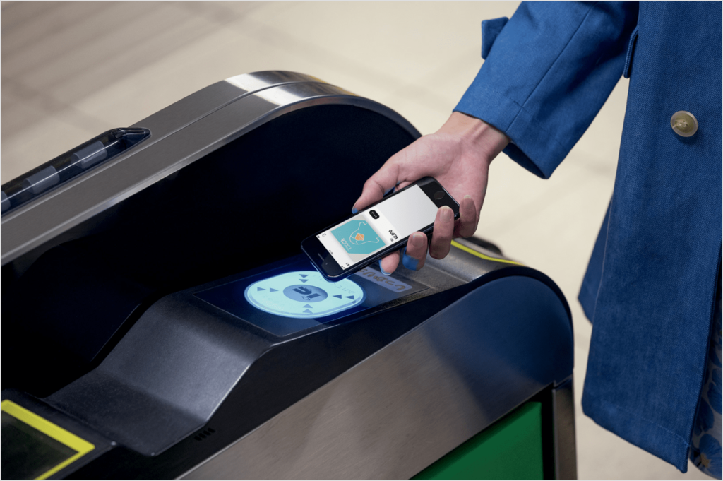 A person holding their iPhone with the ICOCA card on display near the ticket gate scanner.