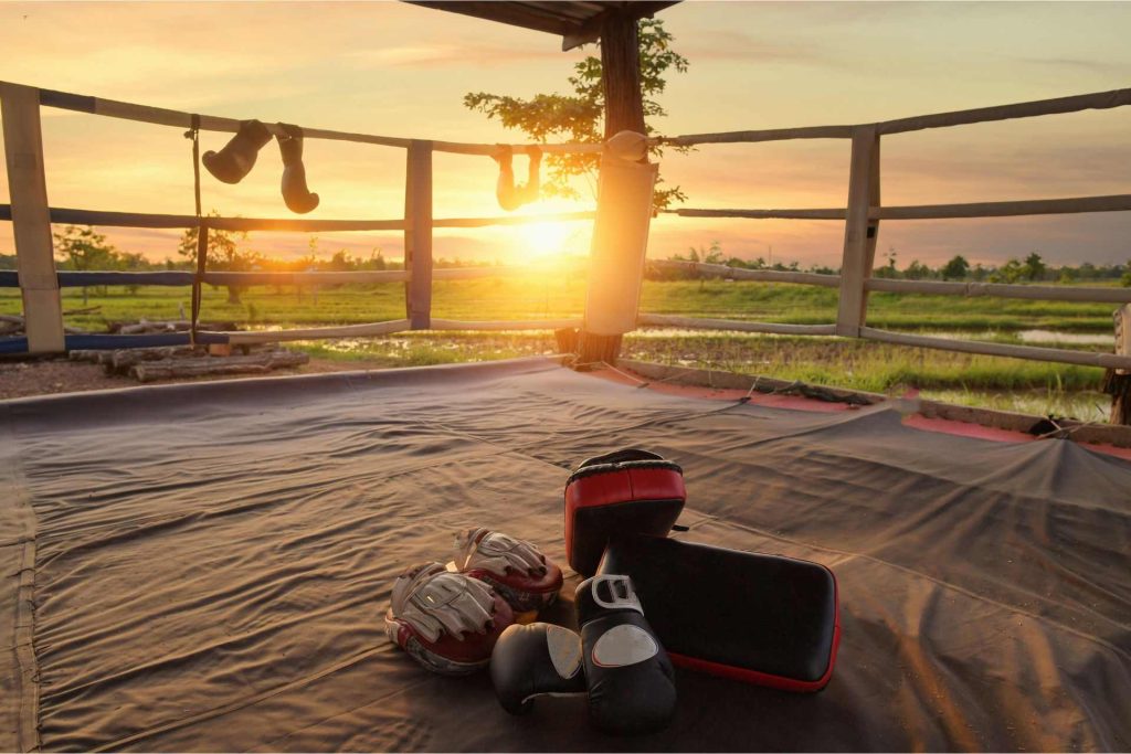 Muay Thai gloves and pads on a ring in front of a sunet