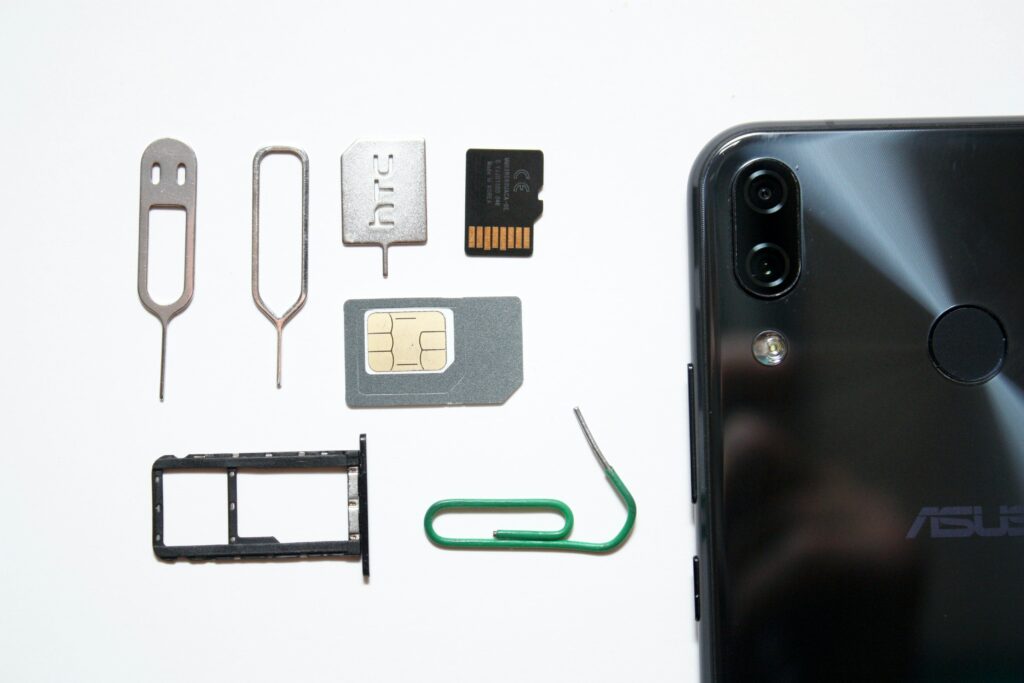 Smartphone with the SIM card and memory card removed, with the SIM tray placed next to various SIM ejection tools, including a paper clip