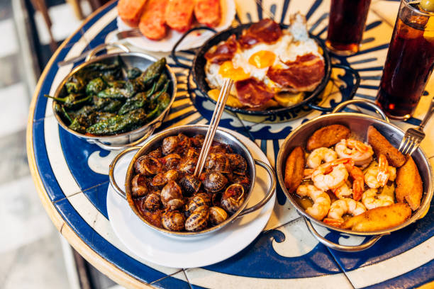  A Spanish tapas platter on a blue table with Caracoles snails, shrimps with garlic, and padron peppers.