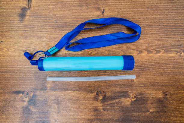 A photo of a blue portable water purifier and a straw on a brown table.