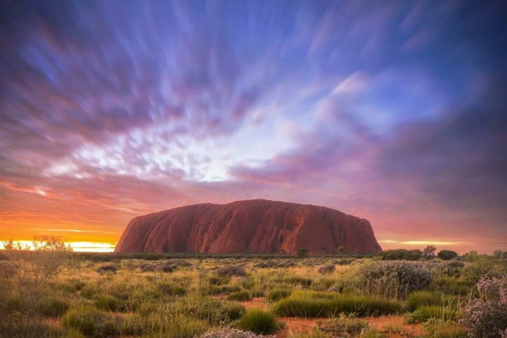 Uluru (Ayers Rock) surrounded by the red desert landscape under a clear blue sky in the Australian Outback.