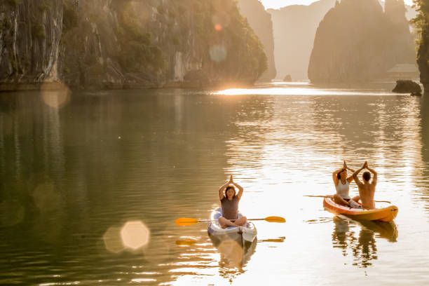 A single tourist and a group of two tourists sitting cross-legged and meditating on a Kayak in Lan Ha Bay, Vietnam.