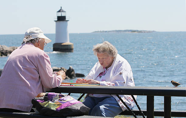 Two people playing cribbage with the Fort Pickering Lighthouse in the background. Source: Getty Images