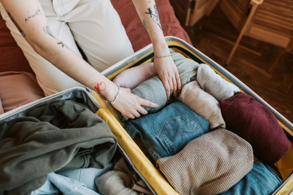 Woman packing rolled knitwear into a suitcase to use for layering on a winter trip.