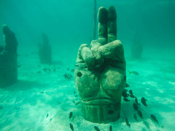 Large stone hands acting as artificial reefs to attract fish in the Cancun Underwater Museum.