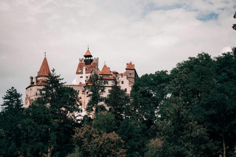 Bran Castle in Transylvania, surrounded by a lush forest beneath a cloudy sky.
