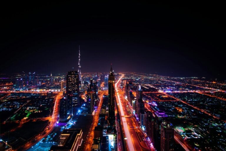 Aerial view of Dubai with its highways and skyscrapers lit up at night.