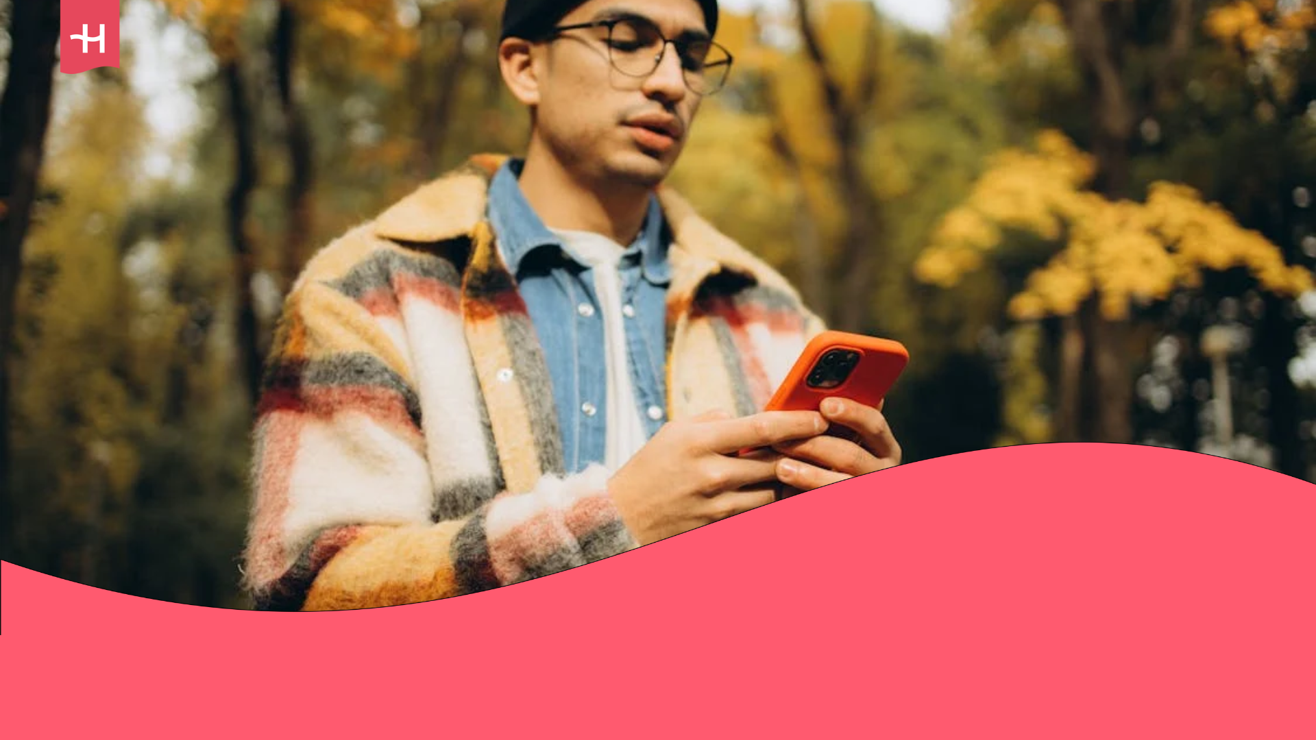 Young traveler holding a mobile device with an orange protective case against a blurry background of a forest in the fall.