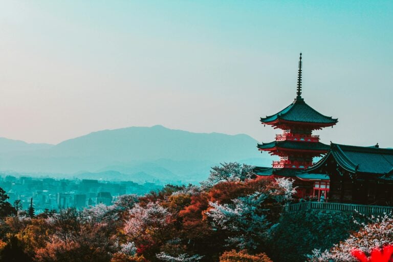 Red and black temple surrounded by trees with vibrant fall foliage, set against foggy mountains in the background