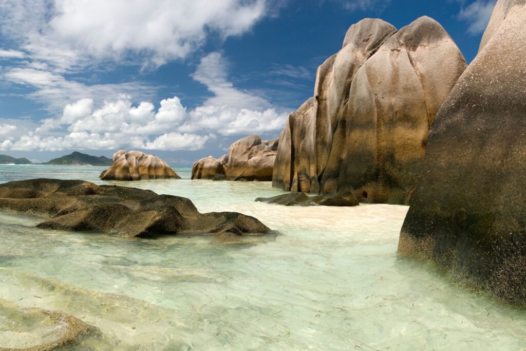 The large rocks of Anse Source D'Argent beach in the water and clouded and sunny sky.