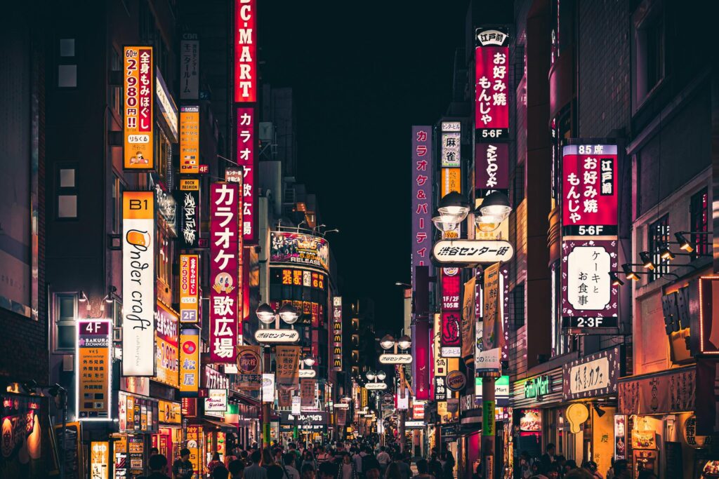 A street lit up with neon boards in the Shinjuku district of Tokyo.
