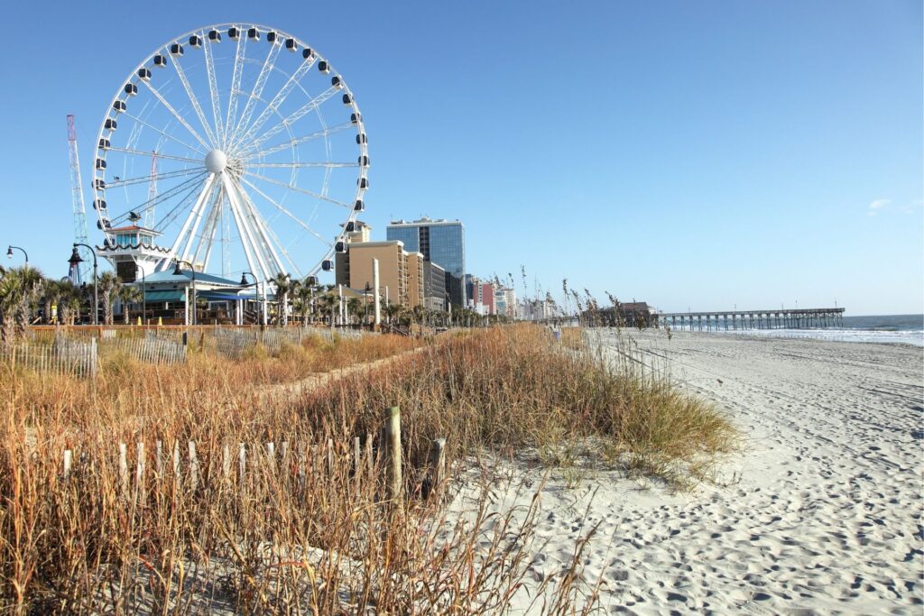 Shot of Myrtle Beach's boardwalk ferris wheel, and beach against a sunny and blue sky.