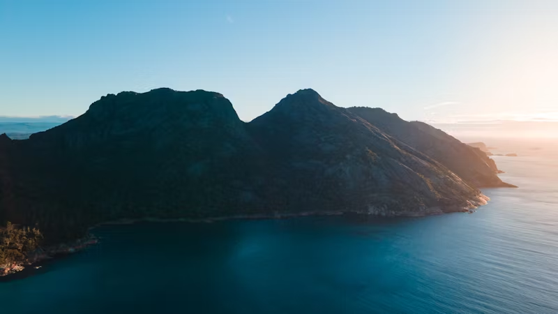 Aerial view of Wineglass Bay Beach with tall, steep hills surrounded by calm ocean waters.
