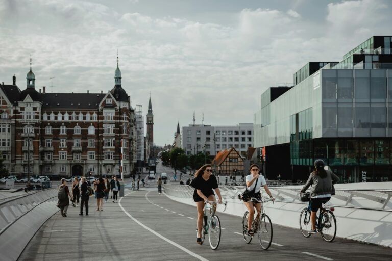 Pedestrians and bikers on a bridge in Copenhagen, with a mix of old and modern architecture in the background.
