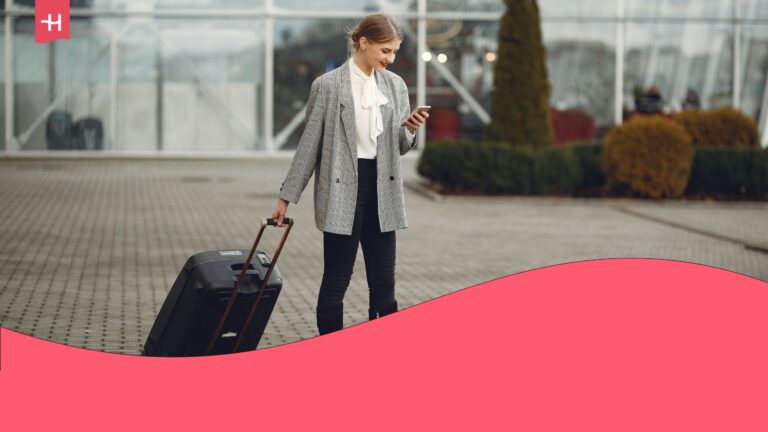 A woman leaving the airport at her destination, holding the handle of her carry-on luggage while checking her mobile device.