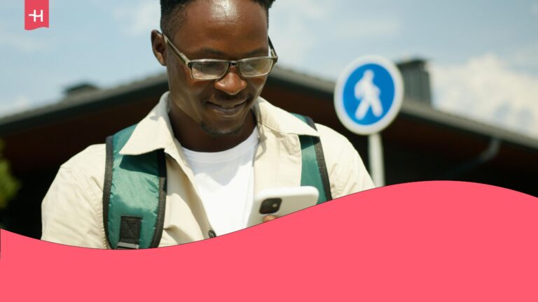 A traveler carrying a backpack, looking at his smartphone and smiling, excited for his travel plans.