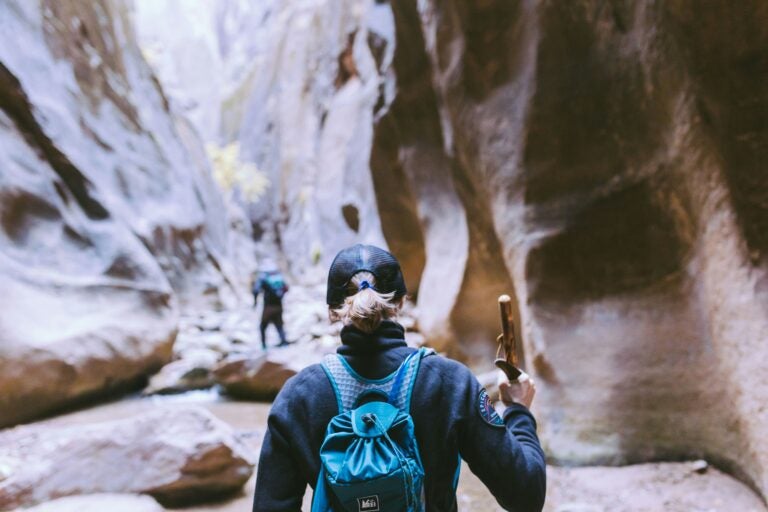 Hikers exploring Zion National Park, Utah, using walking sticks to navigate rocky terrain in a deep canyon.
