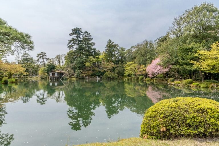 A lush green garden's reflection mirrors on the surface of a lake in Kanazawa, Japan 