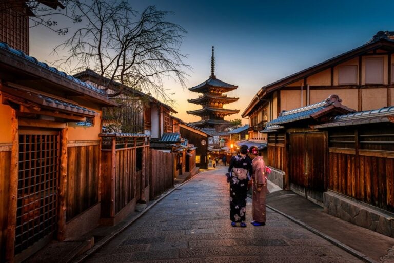 Two geishas stand on a secluded, dimly-lit street in Kyoto, Japan