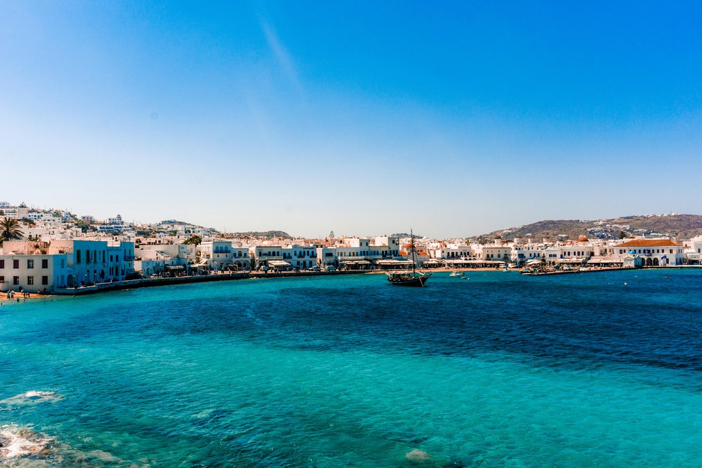 Calm turquoise blue waters with small house-like structures in the background against a blue sky 