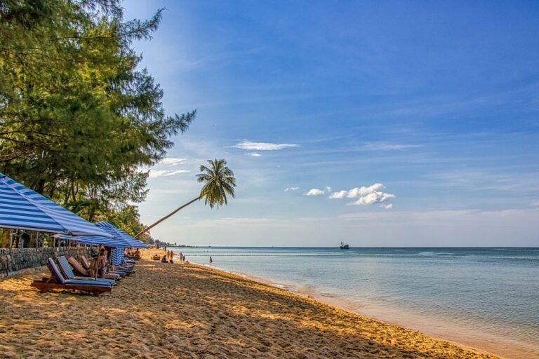 Striped beach umbrellas and sun chairs are lined on golden sands on a beach in Phu Quoc Island, Vietnam