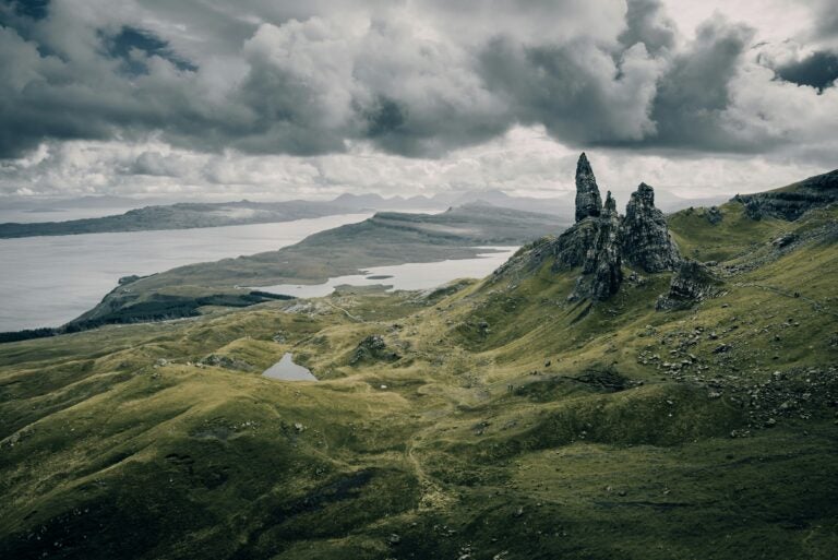 The Scottish Highlands, with rolling hills, sparse rock formations, and a lake in the background.
