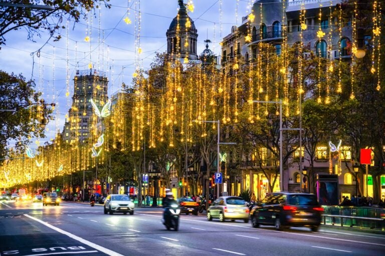 Evening shot of Passeig de Gracia in downtown Barcelona with Christmas lights and decorations along the avenue and cars driving up and down the street.