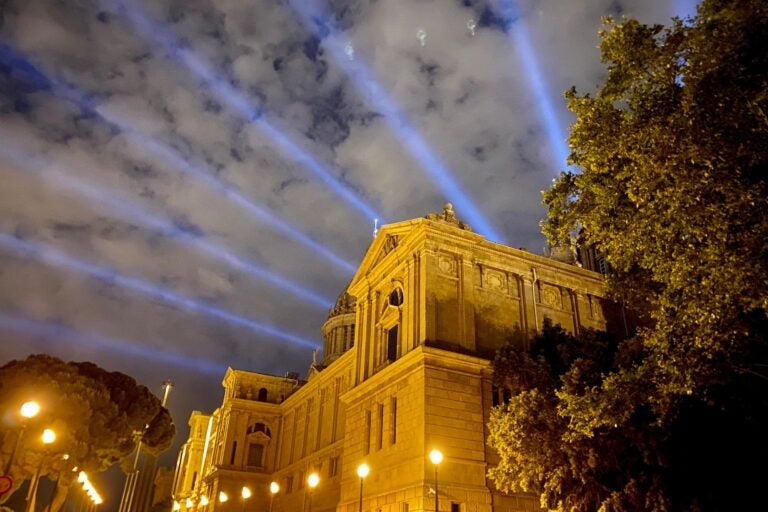 Night shot of Montjuïc Castle with laser lighting coming through from behind.