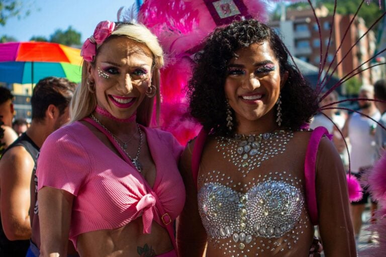 Day shot of Barcelona Pride parade. Two people dressed up in colorful sparkling clothing.