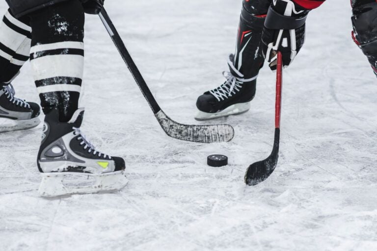 Two people in full hockey gear facing each other, with a hockey puck between them, and they're holding hockey sticks.