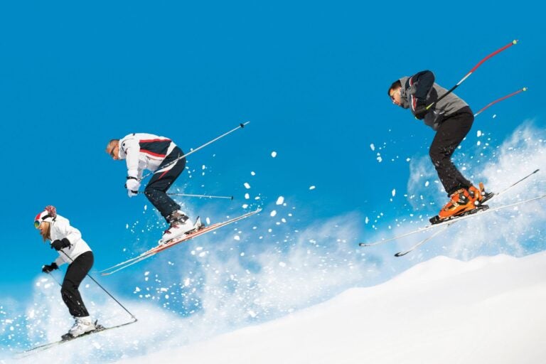 Two men and one woman skiing down a slope on a sunny blue sky day.