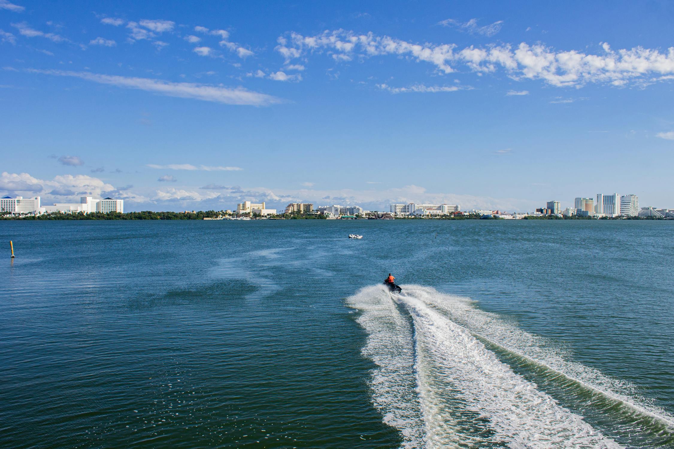 An aerial shot of a person driving a jet ski towards the shore in the distance.