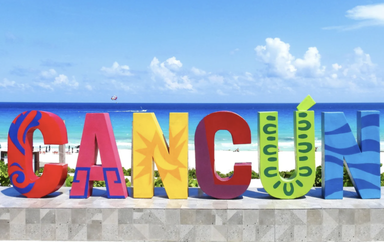 Closeup frontal shot of the "Cancun" sign in front of the beach on a sunny day