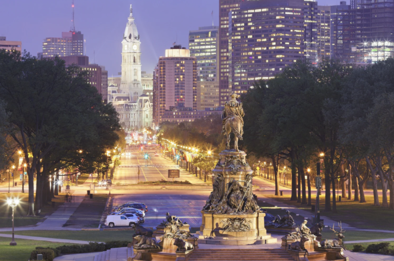 Evening shot of a wide Philadelphia city street with a statue in the centre of the shot.