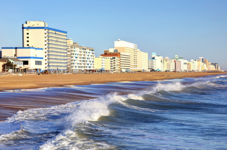 Side shot of Virginia beach and on a sunny and blue sky day, with building dotted along the shoreline.