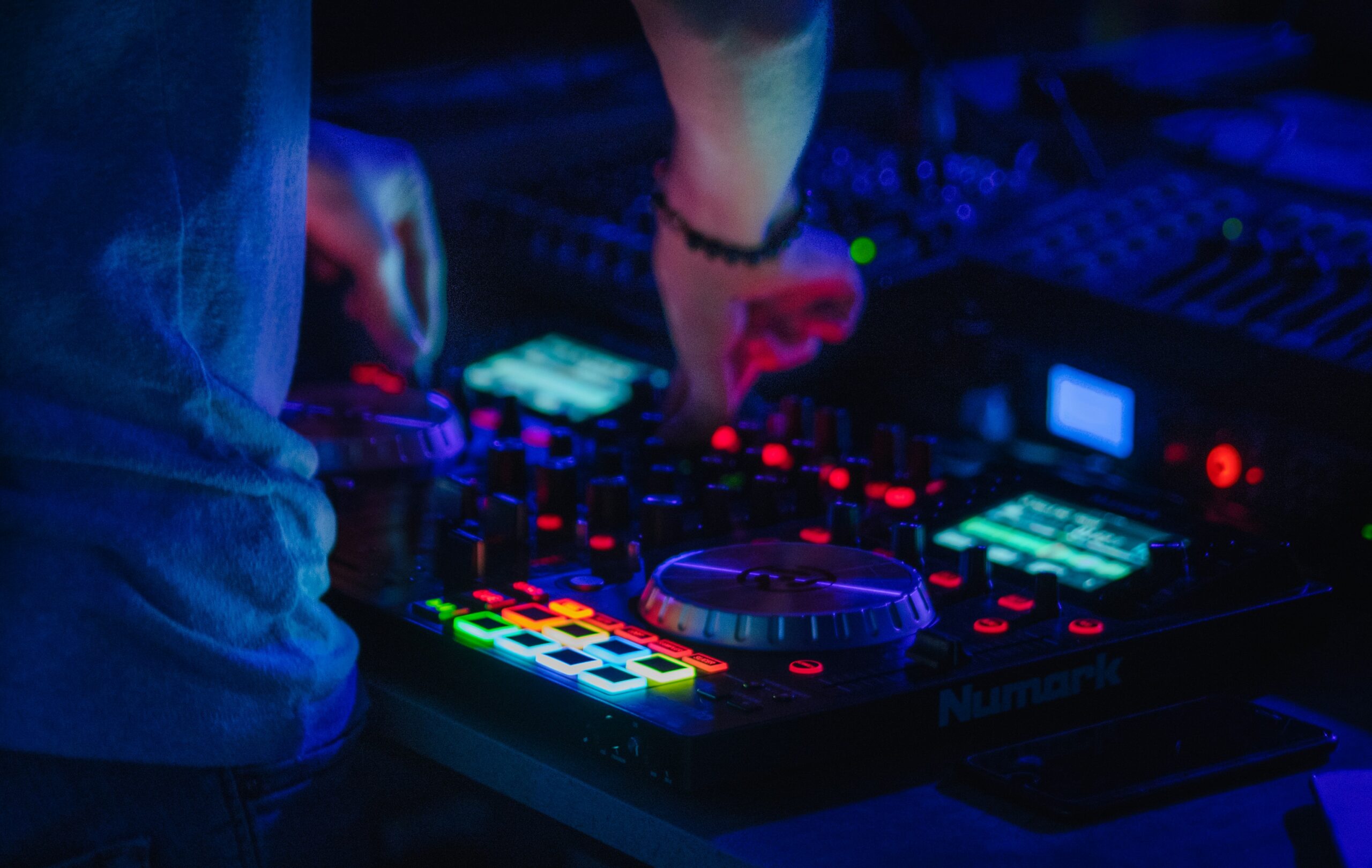 A dsark image of a DJ's hands adjusting the knobs on a deck.