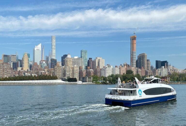 a ferry whizzing by in front of the New York City skyline