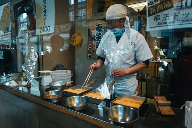a man preparing food in a food stall behind a glass barrier